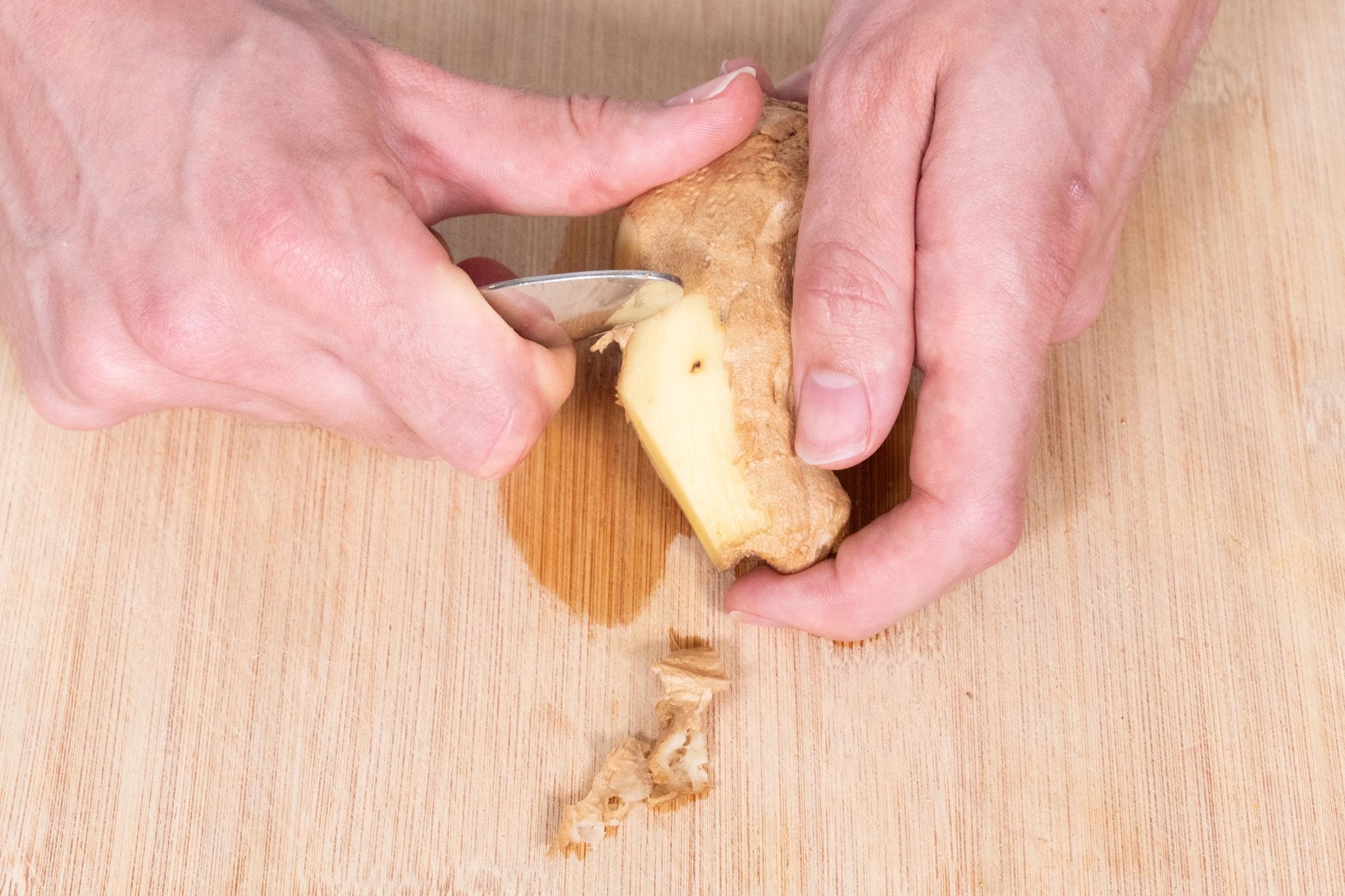 Der Ingwer wird mit der einen Hand festgehalten. In die andere Hand nimmt man die Mulde eines Teelöffels, so dass man mit der Innenseite gut kratzen kann.
