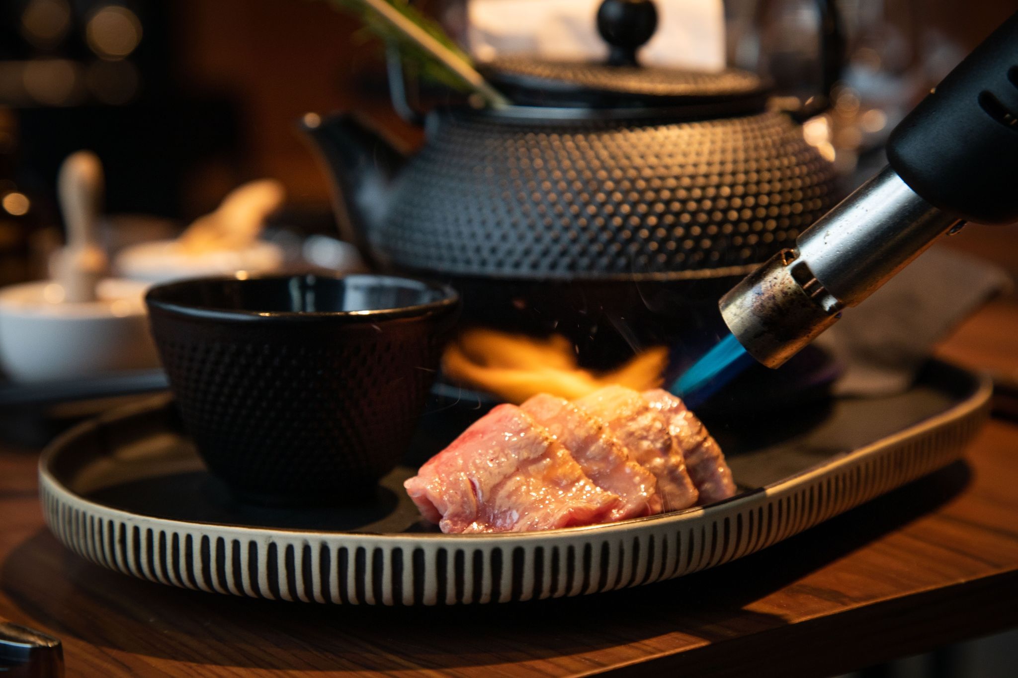 Vier dünne Scheiben vom Wagyu-Beef werden mit dem Flambierbrenner angeröstet.