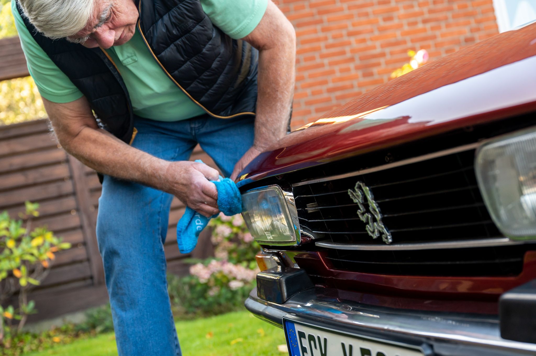 Ein Mann reinigt die Scheinwerfer seines Peugeot 504 Coupé-Oldtimers. Unter Umständen kann man das Licht auf modernes LED-Licht aufrüsten, ohne den Oldtimerstatus zu verlieren.