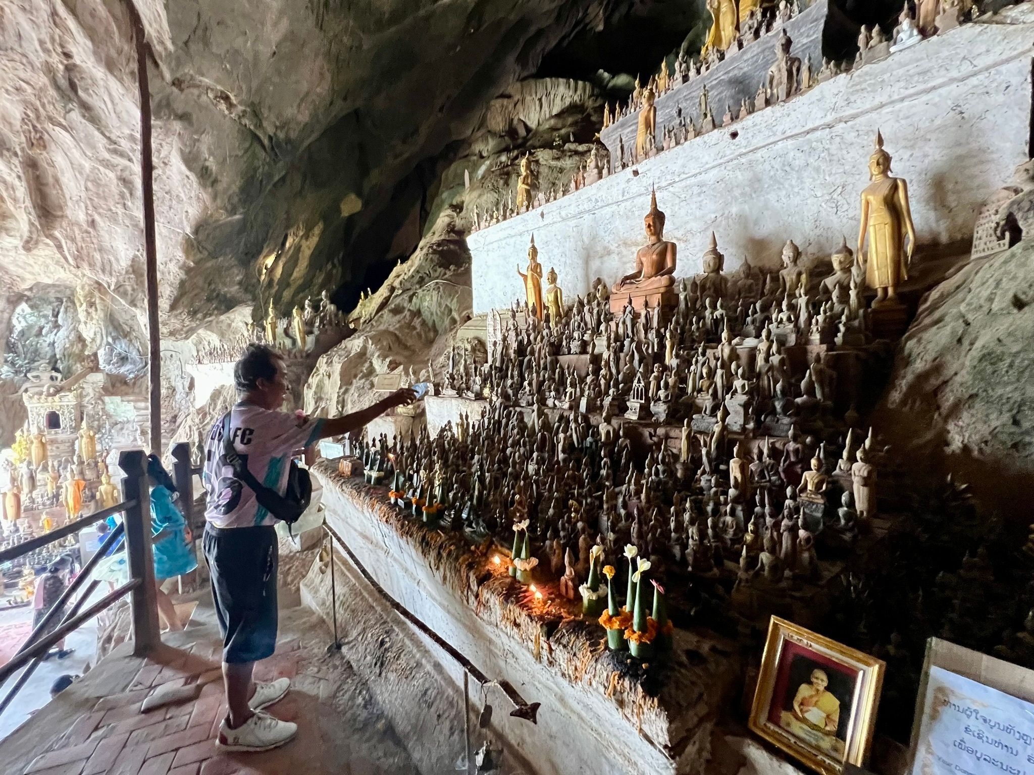 Ein Mann besprenkelt Buddha-Statuen in den Pak Ou Caves als Zeichen des tiefen Respekts mit Wasser.