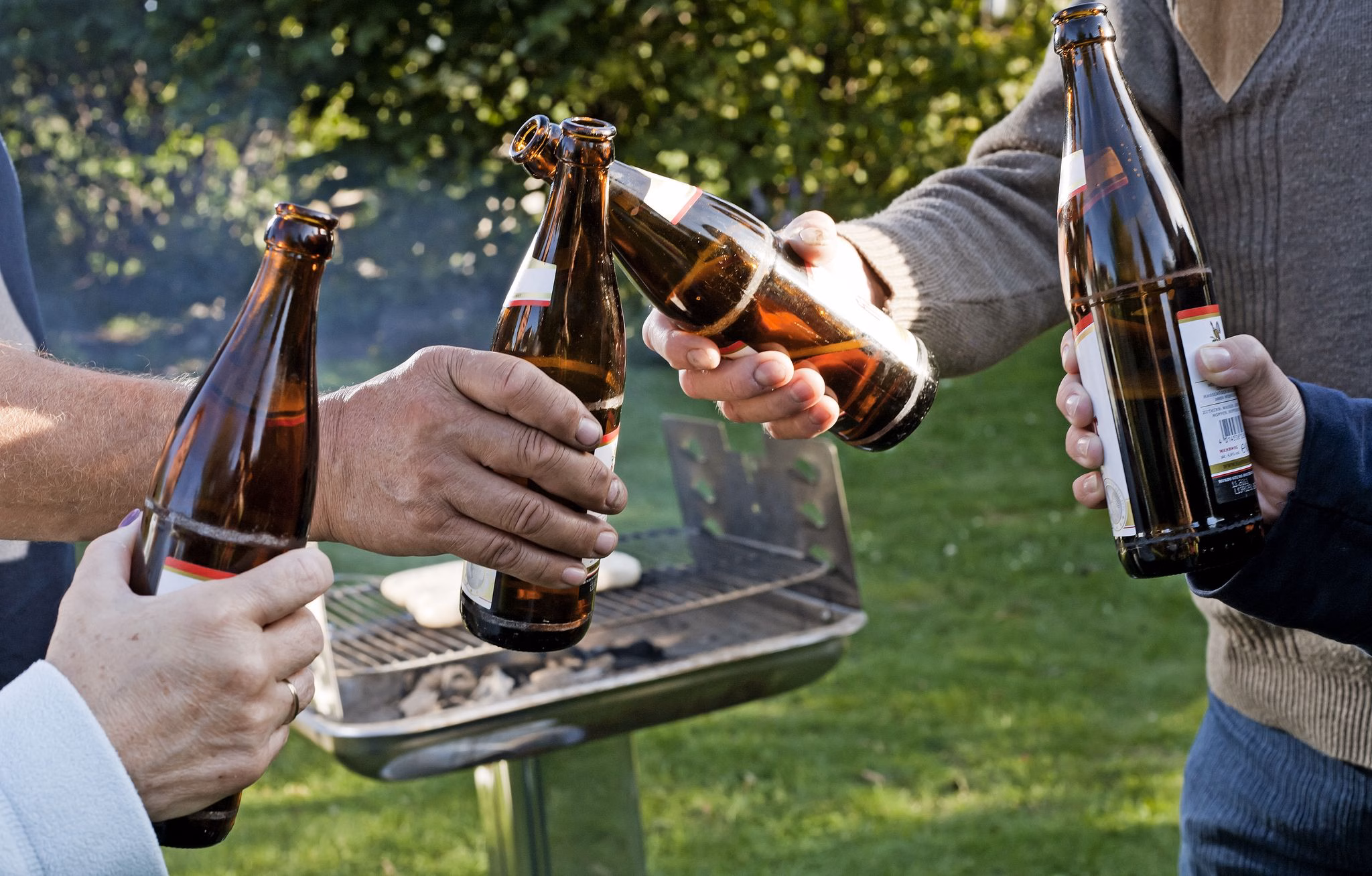 Vier leute stoßen draußen vor einem grill mit bierflaschen an